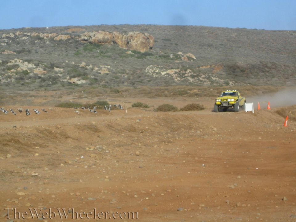 Yellow off-road truck on a distant dirt course lined with cones and tires
