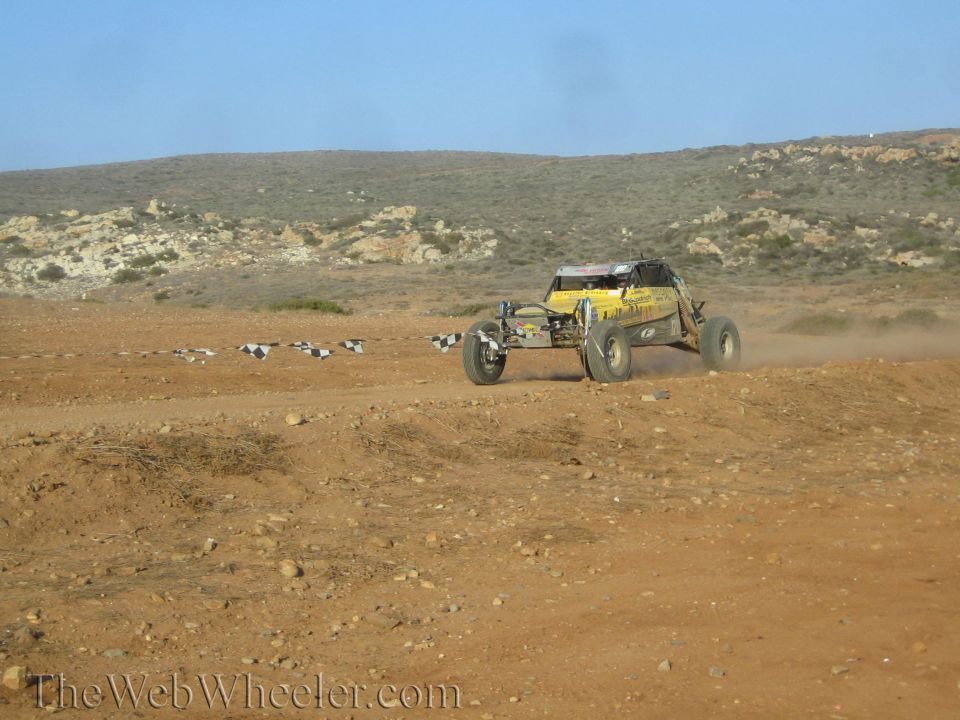 Yellow off-road buggy racing on a desert dirt track lined with tires