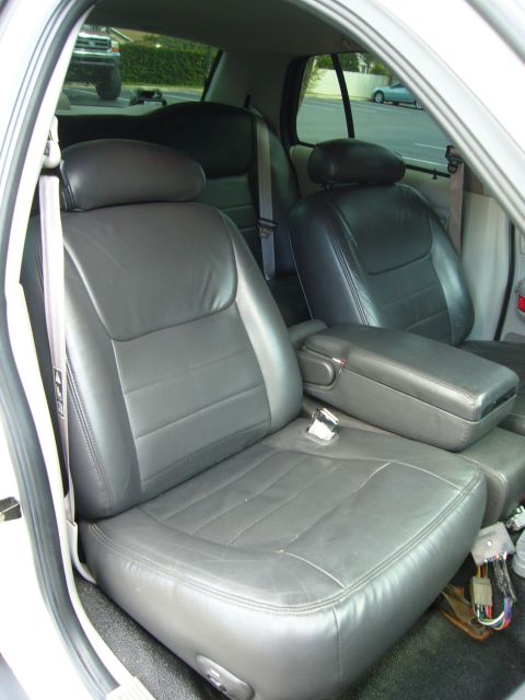 2000 Ford Crown Victoria - Interior shot through the open passenger door of a white sedan showing gray leather front bucket seats with a fold-down center console armr…