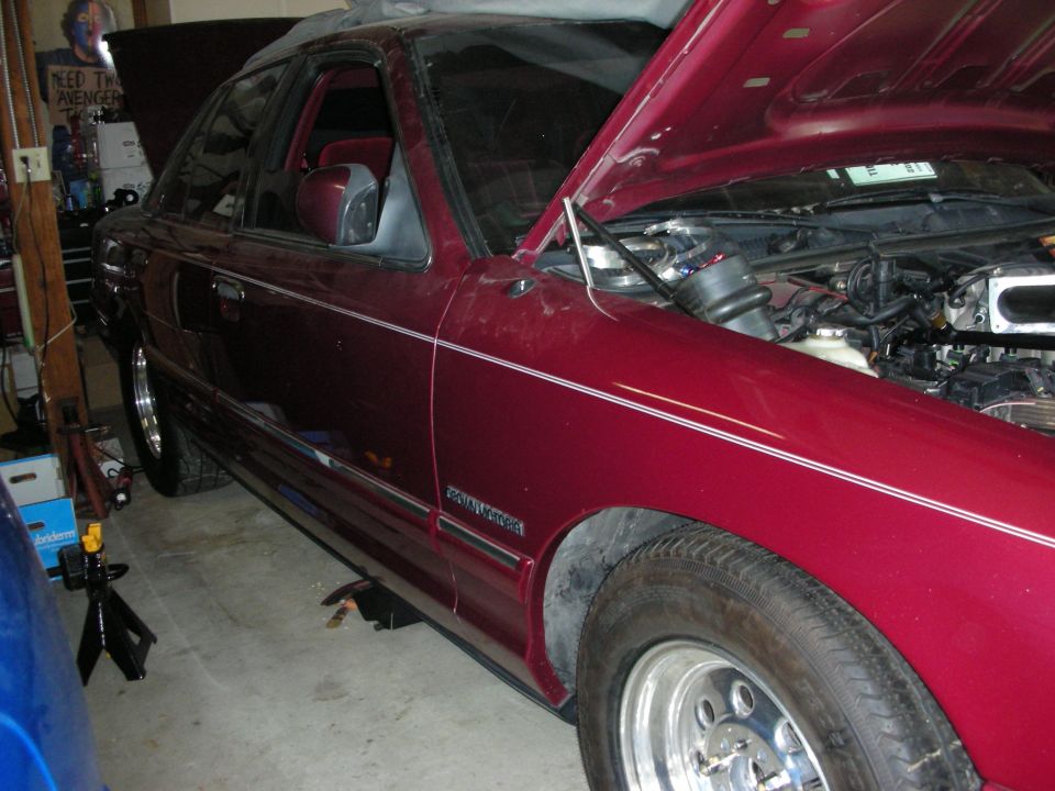 Maroon 1992 Ford Crown Victoria with hood open, showing engine bay. Car is on jack stands in a garage