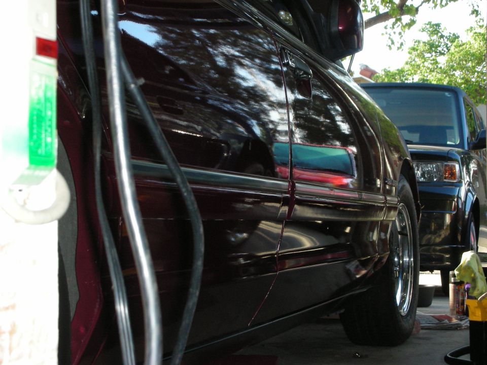 Dark red sedan side view, chrome trim, reflection of trees and another vehicle