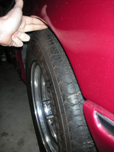 1992 Ford Crown Victoria - A hand is shown measuring the clearance between a red car's fender and tire, suggesting a modification or inspection.