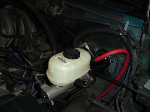 1996 Ford Bronco - Close-up view of a brake master cylinder with a visible label and red hose.