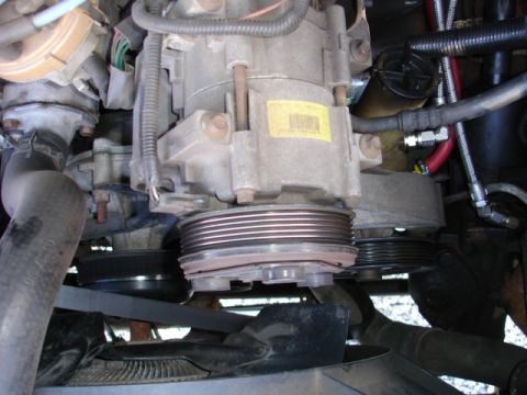 1996 Ford Bronco - Detail of the air conditioning compressor and associated pulleys within an engine compartment.