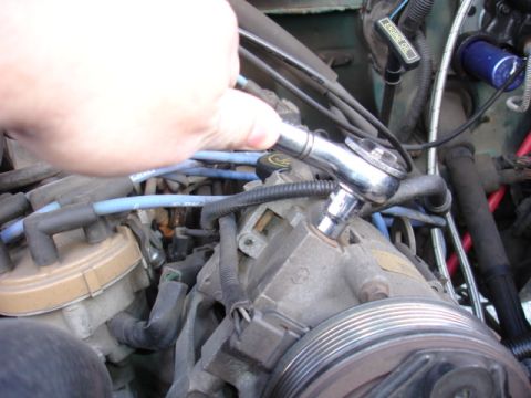 1996 Ford Bronco - A hand is using a socket wrench on a component in the engine bay, surrounded by wires and hoses.