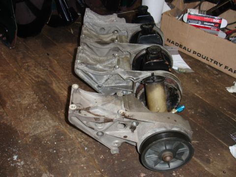 1996 Ford Bronco - Multiple power steering pump assemblies are laid out on a wooden surface.