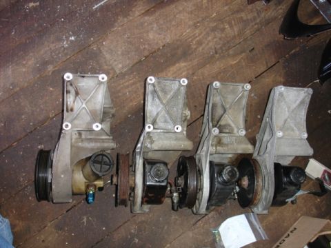 1996 Ford Bronco - A collection of four power steering pumps are laid out on a rustic wooden surface.