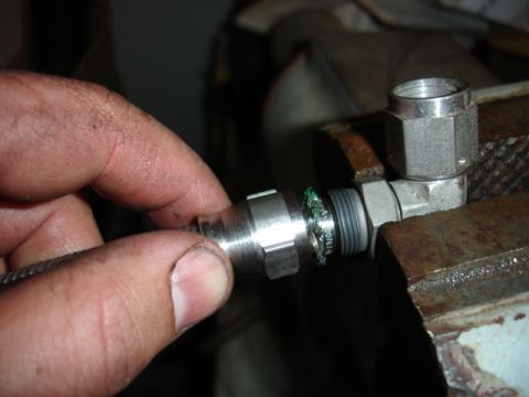 1996 Ford Bronco - A close-up shows a metal fitting being held by a hand and secured in a vise, with visible green sealant around the threads.