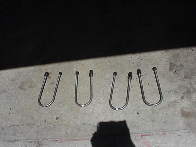 Four U-bolts laid out in a row on a concrete garage floor at night