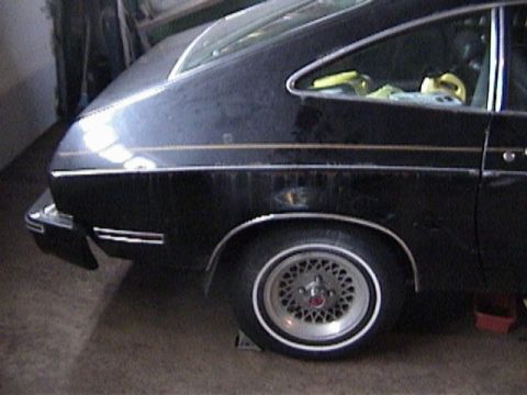 1977 Ford Mustang - Rear quarter view of a black 1977 Ford Mustang II hatchback with gold trim and distinctive wheels.