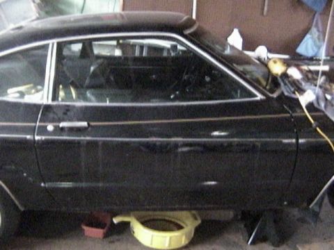 1977 Ford Mustang - Side profile of a black 1977 Ford Mustang coupe, showing its body style and gold trim details.