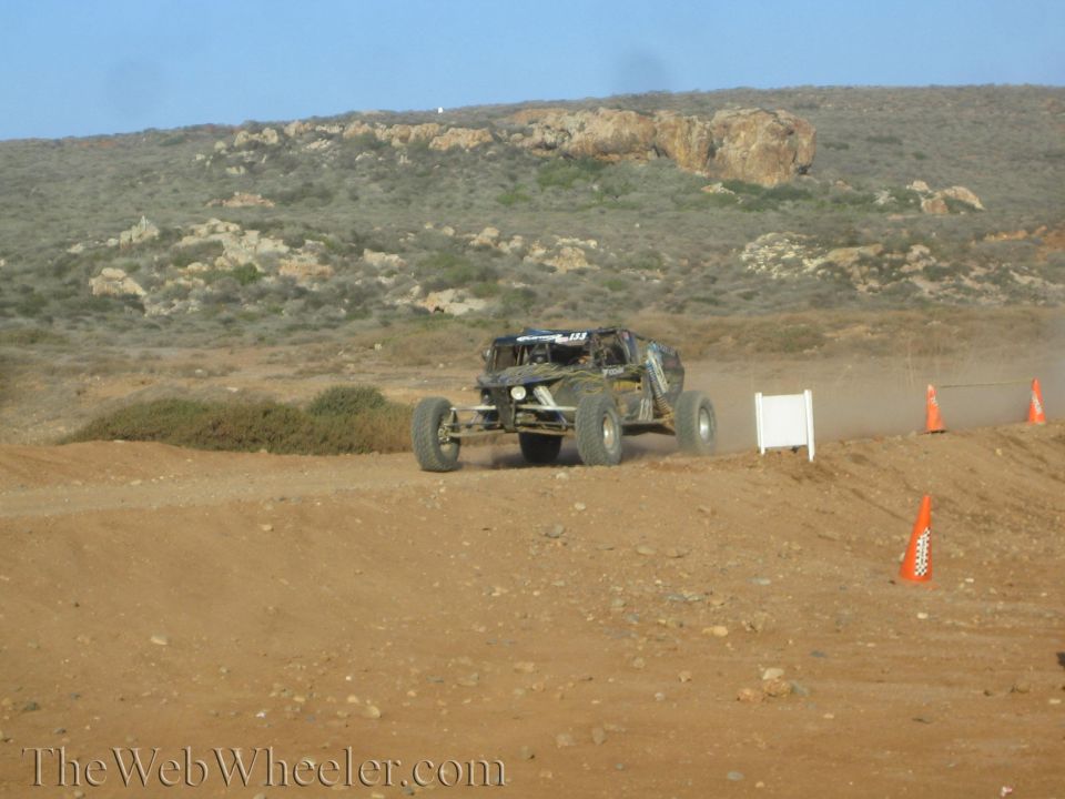 Off-road buggy cresting a dirt berm on a coned desert course