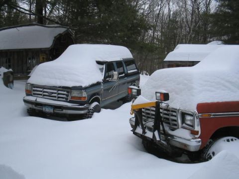 1979 Ford Bronco - Two SUVs are parked in a snowy yard next to wooden structures.