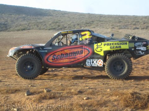 1990 Ford Bronco - black off-road race truck numbered 2 with Schampa and Precision Gear branding sits on a dry grassy hillside.