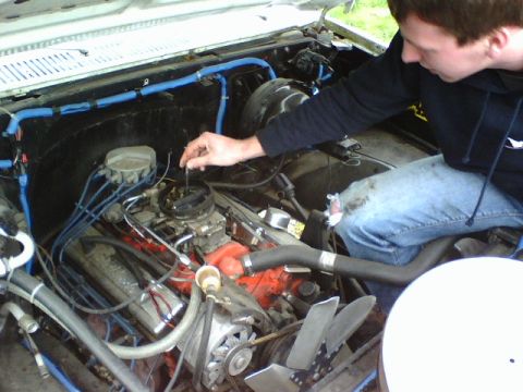 1987 Ford Bronco - A person works on the engine of a vehicle, focusing on the carburetor and V8 engine components.