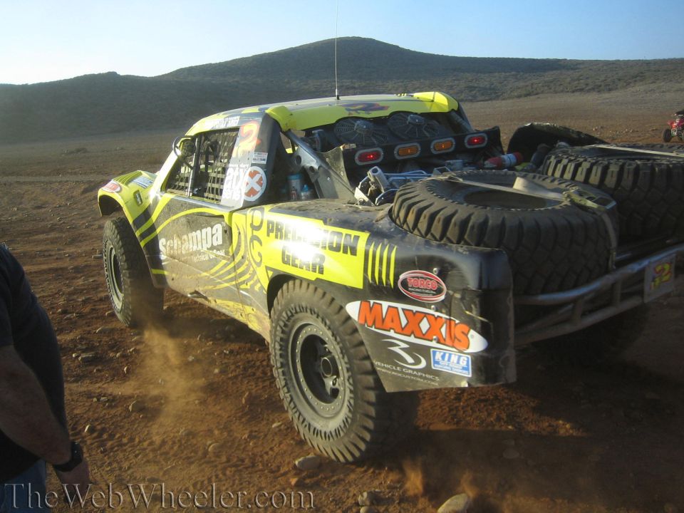 Rear of green-yellow off-road race truck with spare tires in desert