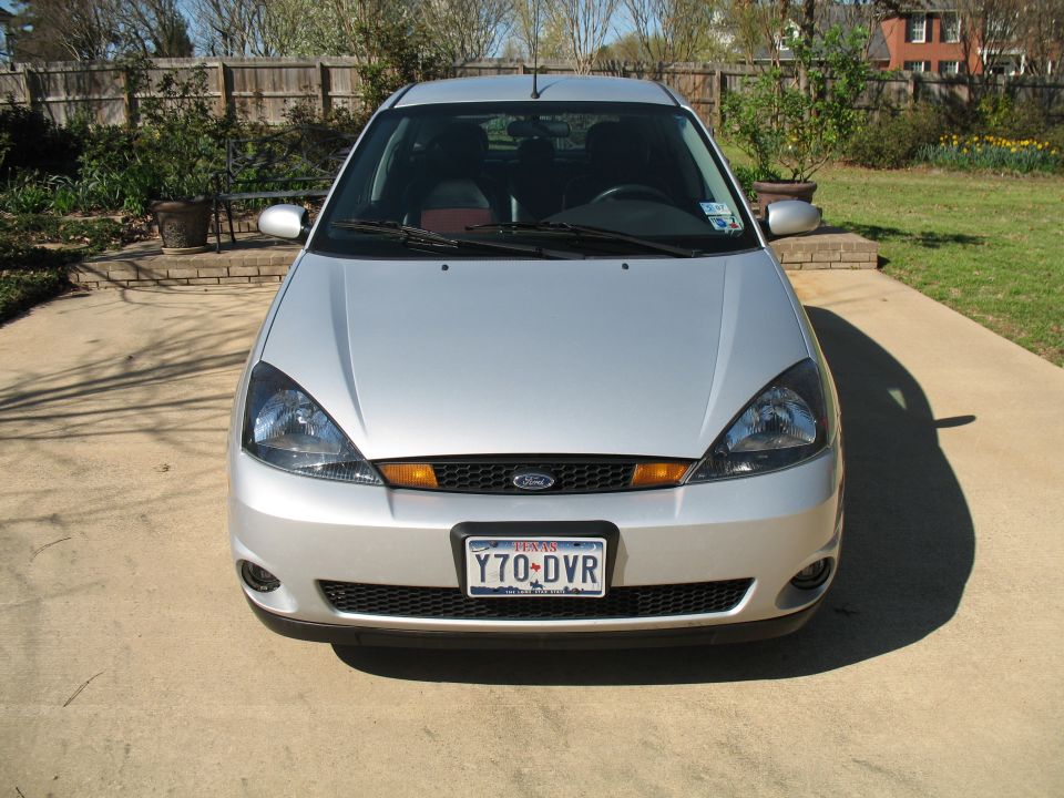 Silver Ford Focus parked on concrete driveway, front view. Black grille with orange accents, Texas license plate Y70-DVR