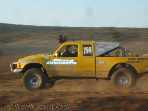 1990 Ford Bronco - yellow off-road race truck numbered 756 with Sierra Brothers Racing and Doug Thorley Headers decals races across the desert.