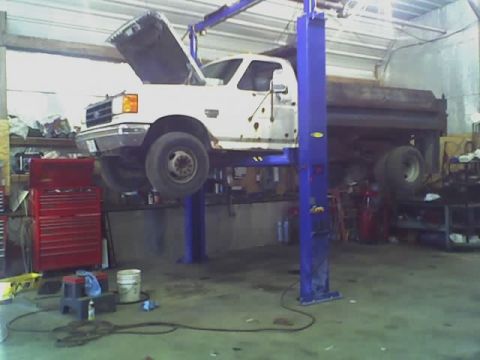 1992 Ford Bronco - A white dump truck is raised on a hydraulic lift inside a garage, with its hood open.