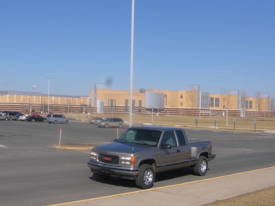 Gray GMC extended-cab pickup parked in a lot near a large building