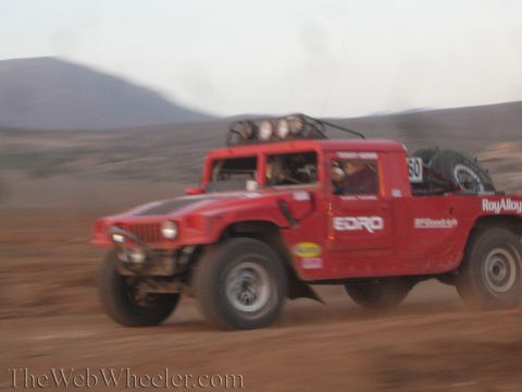 1990 Ford Bronco - red Hummer-style off-road race truck carrying number 50 and 'EDRO' livery races across the desert with motion blur.