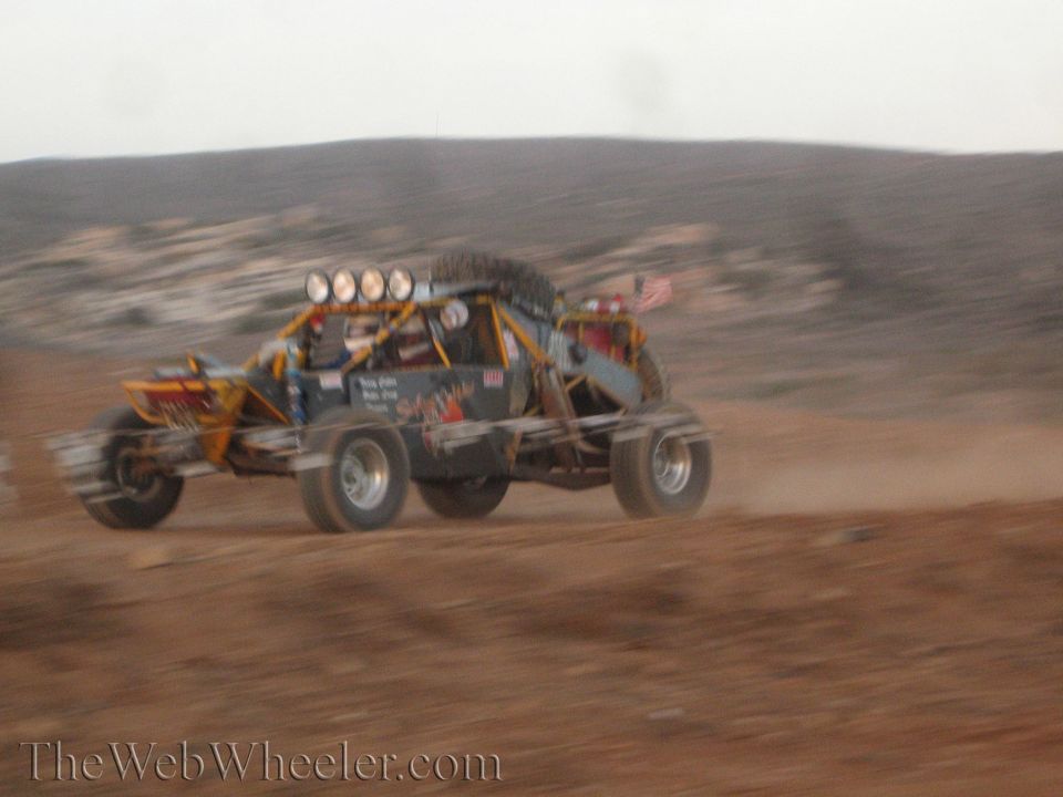 Open tube-frame sand buggy racing across desert dirt
