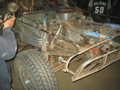 1990 Ford Bronco - photographer documents the muddy exposed tube chassis, suspension and rear engine of an off-road race vehicle at night.