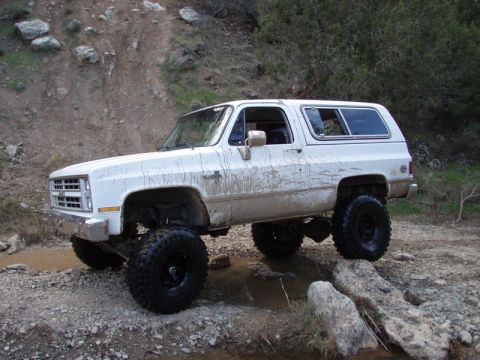 1994 Ford Bronco - This lifted SUV is shown off-roading on a rocky, muddy trail.