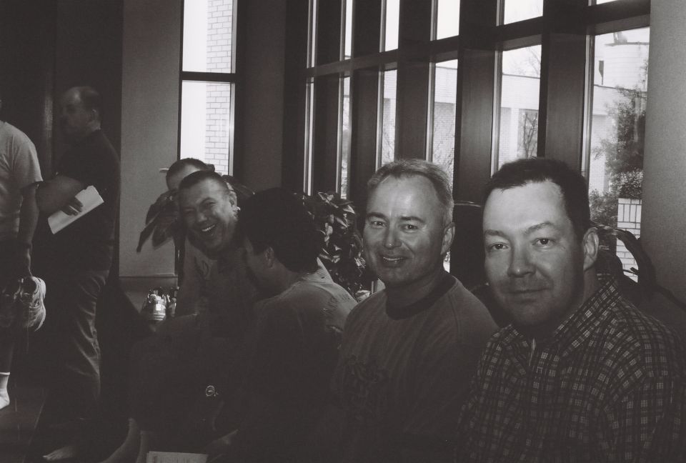 Group of men in a room with large windows, one man laughing, another smiling