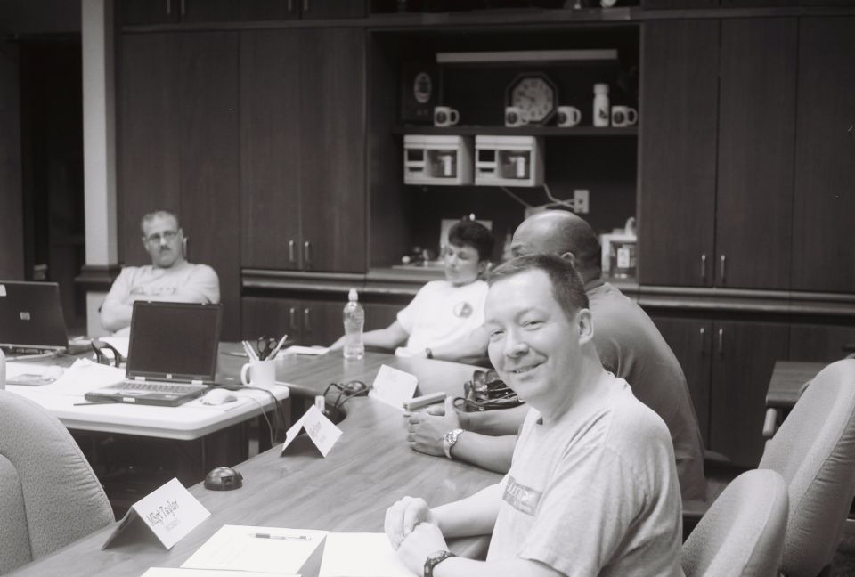 People sitting at a table in a meeting room with laptops and papers