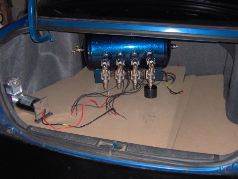 1996 Chevrolet Cavalier - The trunk of a car contains an air compressor and a blue air tank with multiple valves and wiring.