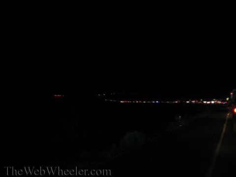 1990 Ford Bronco - very dark nighttime view showing a distant string of colored lights across the landscape alongside a roadway.