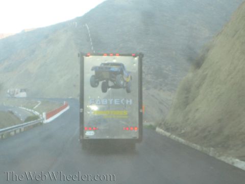 1990 Ford Bronco - black enclosed trailer printed with Fabtech and Toyo Tires off-road truck graphics travels a winding mountain road.