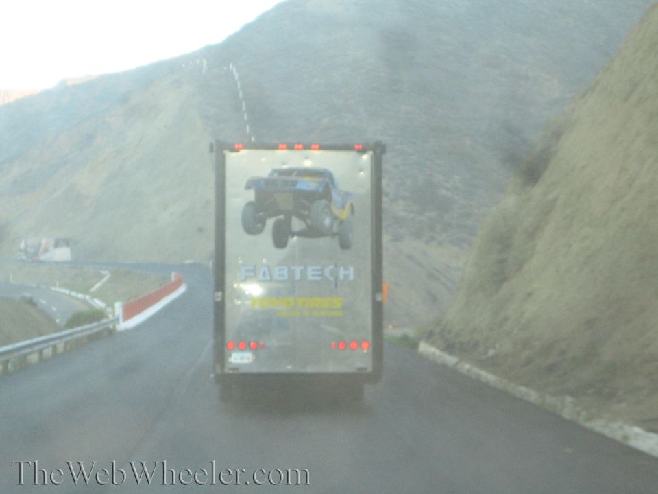 Black Fabtech enclosed trailer with off-road truck graphics on a mountain road