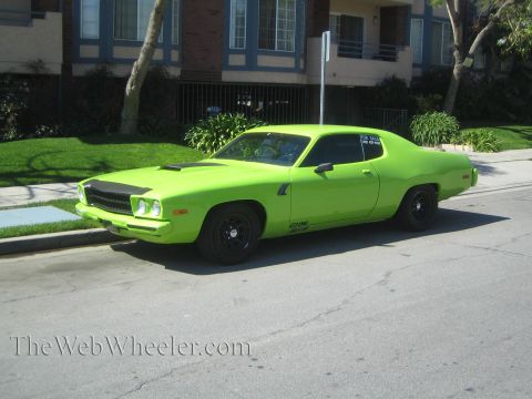 1990 Ford Bronco - lime green 1970s muscle-car coupe with a blacked-out hood and black wheels parks curbside on a sunny residential street.