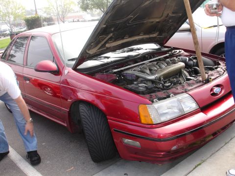 1993 Ford Taurus - A red 1993 Ford Taurus is parked with its hood open, revealing the engine compartment.