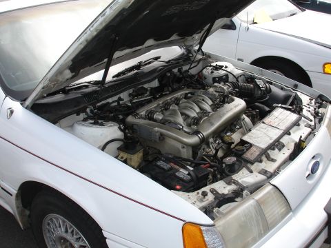 1993 Ford Taurus - The engine bay of a white 1993 Ford Taurus SHO is visible with the hood open, alongside another white vehicle.