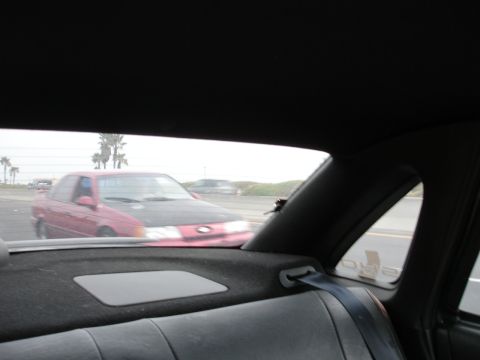 1993 Ford Taurus - A red sedan with a black hood is seen driving on a highway, with other vehicles in the background.