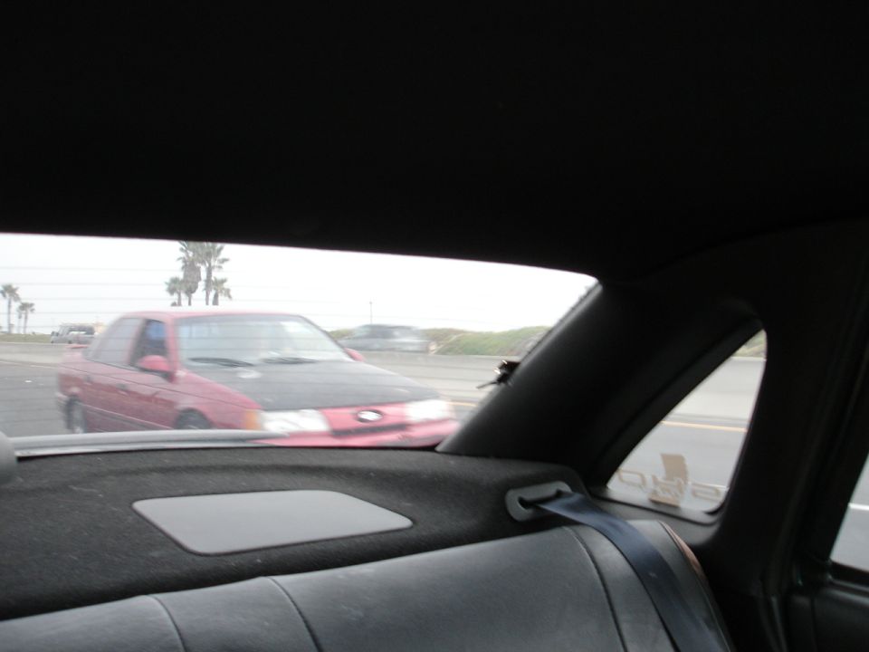 Red sedan with black hood driving on highway, seen from inside another car