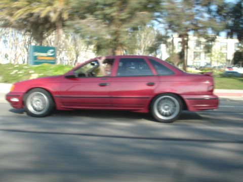1993 Ford Taurus - A red sedan is captured in motion, with a person's hand visible outside the driver's side window.