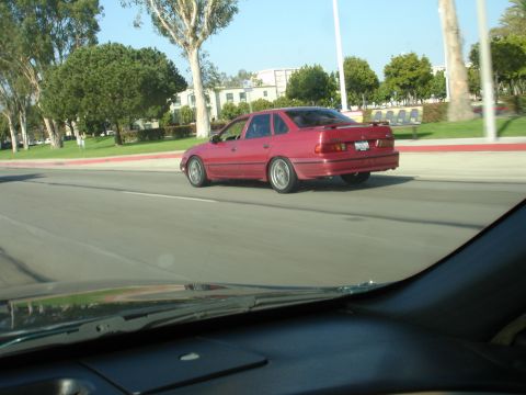 1993 Ford Taurus - A red 1993 Ford Taurus sedan is seen from behind while driving on a sunny day.