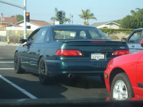 1993 Ford Taurus - Rear view of a 1993 Ford Taurus sedan with aftermarket wheels, seen in traffic next to a red car.