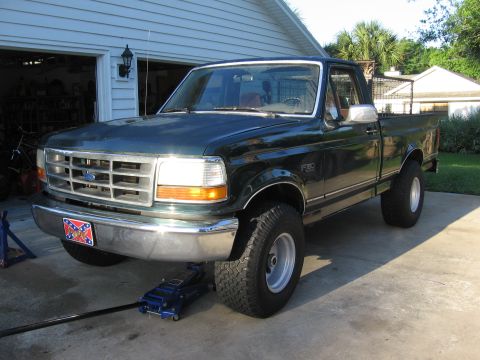 1974 Ford F-100 - A dark green Ford F-150 pickup truck is parked in a driveway with its front end raised by a hydraulic jack.