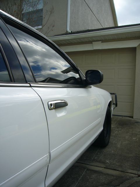 2000 Ford Crown Victoria - The side of a white sedan is visible, parked in front of a closed garage door.