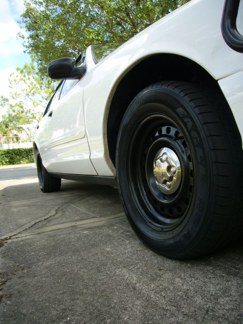 2000 Ford Crown Victoria - The side profile of a white 2000 Ford Crown Victoria is visible, with a focus on the front wheel and tire.