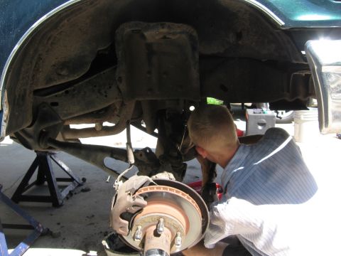 1974 Ford F-100 - A mechanic works on the brake assembly and suspension of a vehicle's undercarriage, supported by jack stands.