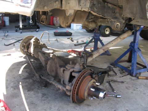 1974 Ford F-100 - The front suspension and axle of a truck are disassembled and supported by jack stands in a workshop.