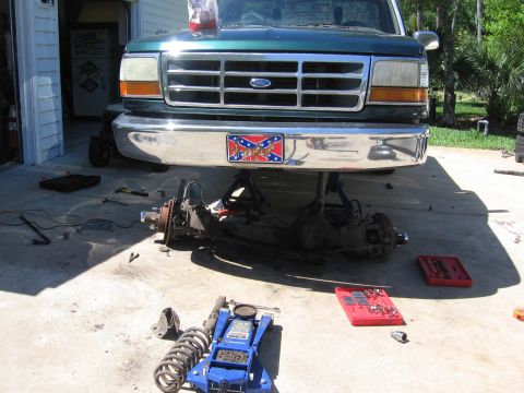 1974 Ford F-100 - Front suspension of a green Ford truck is being worked on, with parts laid out on the ground.
