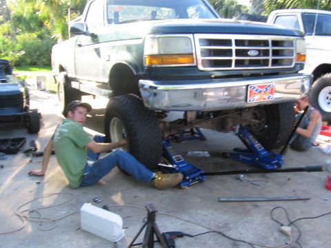 1974 Ford F-100 - A green 1995 Ford F-150 is shown with its front end lifted on jacks, as two individuals work on the suspension.