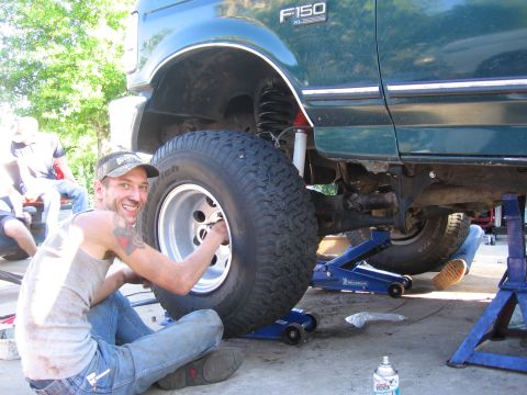1974 Ford F-100 - Man works on a green Ford F-150 XL truck lifted on jacks, with another person assisting underneath.